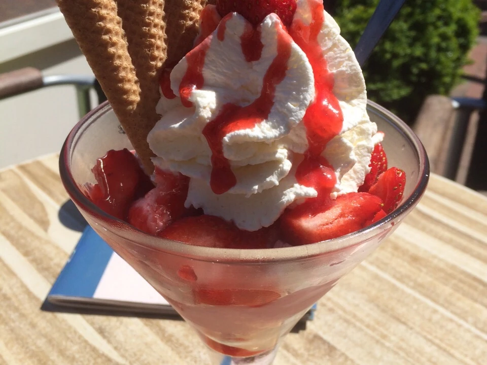 Erdbeer-Eisbecher mit Sahne, Erdbeeren, Waffeln und Soße in einem Café an einem sonnigen Tag.