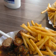 Currywurst Pommes Leckere Currywurst mit knusprigen Pommes, serviert in einer Pappschale mit Plastikgabel.