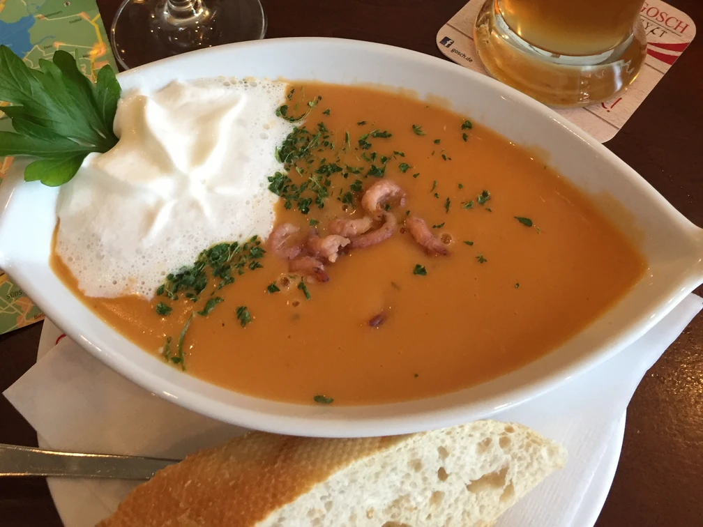 Fischsuppe Cremige Fischsuppe mit Meeresfrüchten und Sahnehaube, serviert mit frischem Baguette auf einem Tisch.