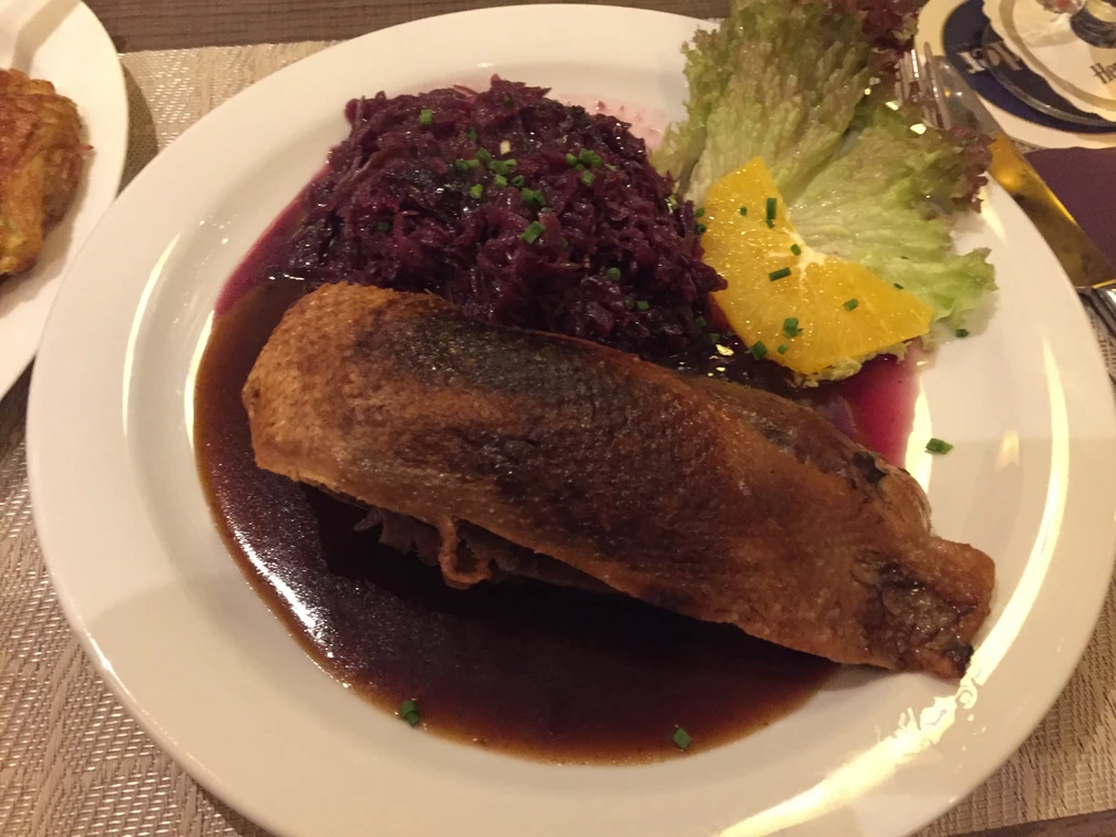 Entenbrust auf einem Teller mit Rotkohl, Orangenscheibe und Soße, serviert mit Salatgarnitur.