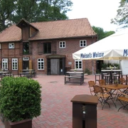 Backsteingebäude mit rotem Dach und Holzelementen, umgeben von Bäumen und Außensitzbereich.