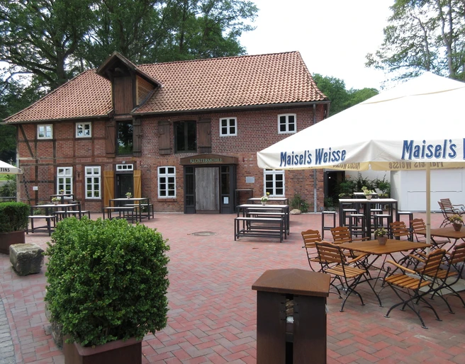 Backsteingebäude mit rotem Dach und Holzelementen, umgeben von Bäumen und Außensitzbereich.