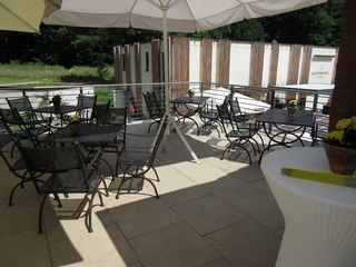 Überdachte Terrasse der Klostermühle Heiligenberg mit leeren Tischen und Stühlen bei sonnigem Wetter.