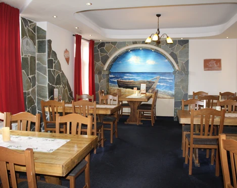 Restaurant Platon Griechisches Restaurant mit Holzmöbeln und Wandgemälde eines Bootes am Strand im Innenbereich.