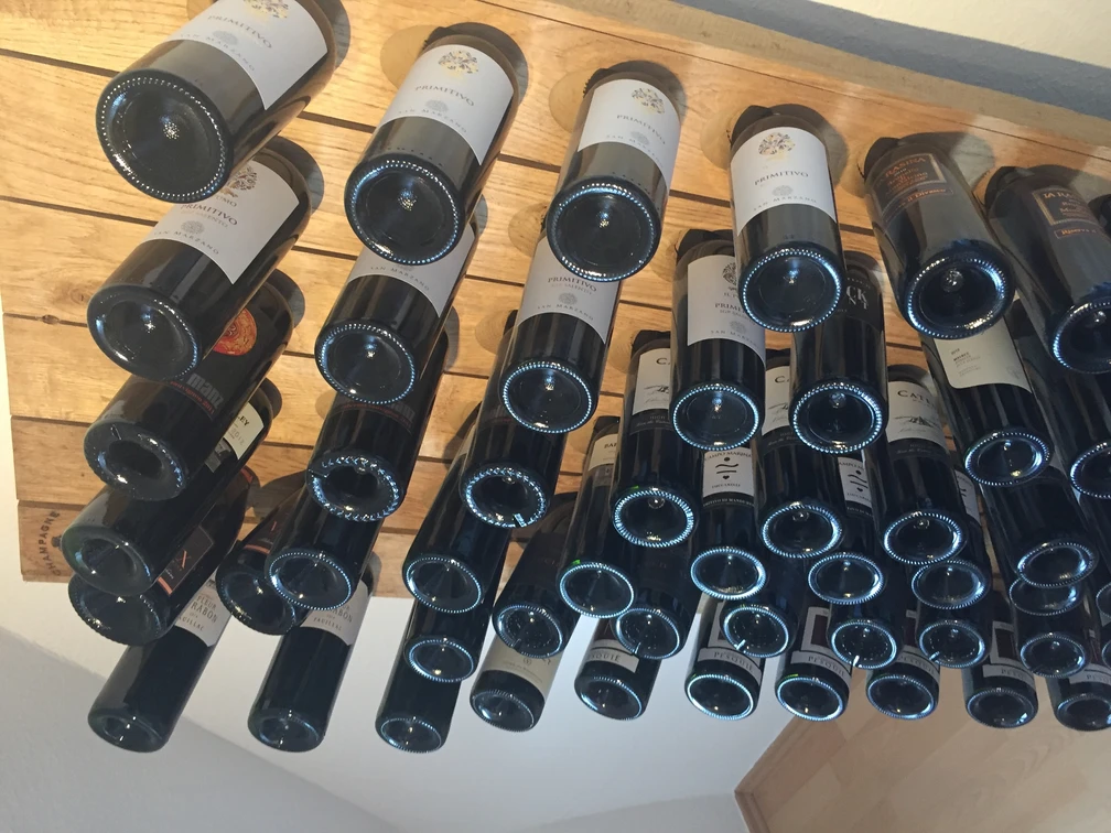 Weinregal Eine Vielzahl von Weinflaschen lagert waagerecht in einem Holzregal mit Blick auf die Flaschenböden.