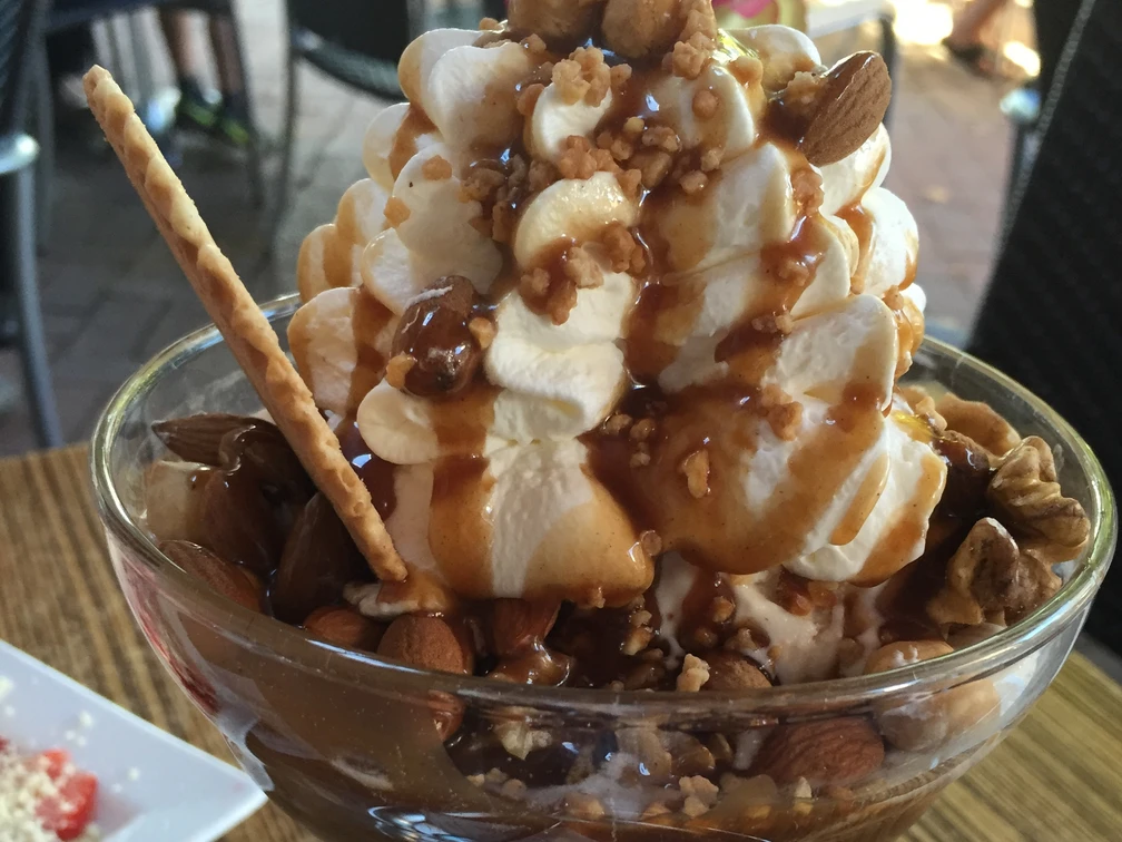 Nussiger Eisbecher mit Sahne, Karamellsauce, Nüssen und dekorativer Waffel auf Holztisch serviert.