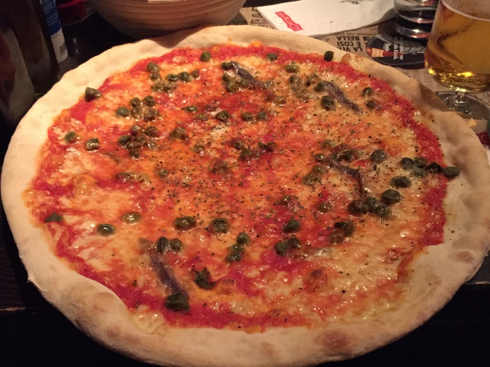 Pizza  Große Pizza mit dünnem, knusprigem Boden, belegt mit Tomatensauce, Käse, Kapern und Sardellen.