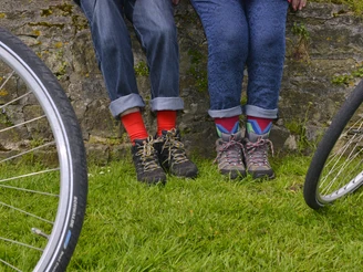 Radeln auf dem OC 1 - Rund um Ostercappeln - Wiegbold, Windthorst und Waldesruh Zwei Personen mit bunten Socken lehnen an einer Mauer, Fahrradräder im Vordergrund.