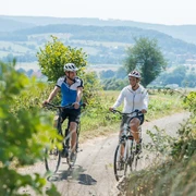 Radfahren mit Blick auf Bad Driburg Zwei Radfahrer genießen eine Fahrt auf einem ländlichen Weg mit Blick auf die sanften Hügel von Bad Driburg.