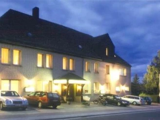 Haus Engemann Mehrstöckiges Gebäude mit beleuchteten Fenstern am Abend, Parkplätze und Fahrzeuge im Vordergrund.