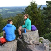 Lippische Velmerstot Zwei Personen sitzen auf Felsen im Lippischen Velmerstot, umgeben von bewaldeter Landschaft.