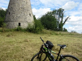 Runder Steinturm auf einer Wiese, im Vordergrund ein abgestelltes grünes Fahrrad, blauer Himmel.