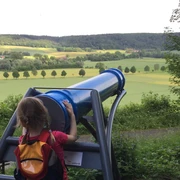 Blick durch das Sphaeriskop Ein Kind betrachtet die weite Landschaft durch ein großes, blaues Sphaeriskop in ländlicher Umgebung.