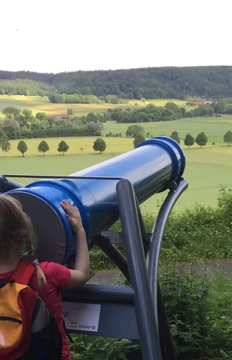 Blick durch das Sphaeriskop Ein Kind betrachtet die weite Landschaft durch ein großes, blaues Sphaeriskop in ländlicher Umgebung.
