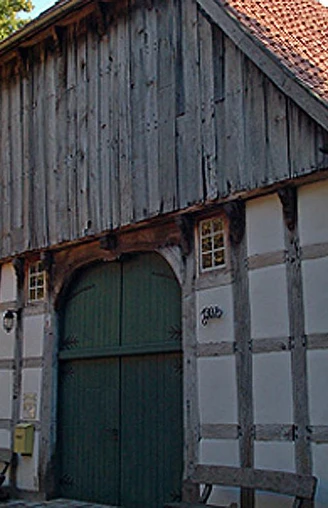 Holzhandwerksmuseum Hiddenhausen Historisches Fachwerkhaus mit großem Holztor und Ziegeldach, umgeben von Bäumen.