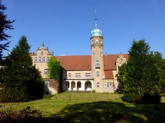 Wasserschloss Ulenburg Historisches Wasserschloss mit markantem Turm, umgeben von gepflegtem Rasen und hohen Bäumen.