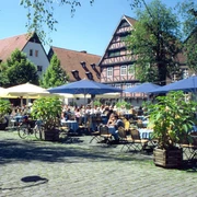 Marktplatz Ein sonniger Tag auf einem Platz, auf dem viele Menschen an Tischen im Freien sitzen und speisen.