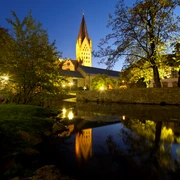 Abendlicher Blick auf den angestrahlten Dom, Kaiserpfalz und Dielenpader, gespiegelt im ruhigen Wasser.