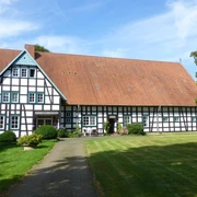 Fachwerkhaus auf gepflegtem Rasen, Hof Oberwahrenbrock, mit großen Dach und weiß-schwarzen Strukturen.