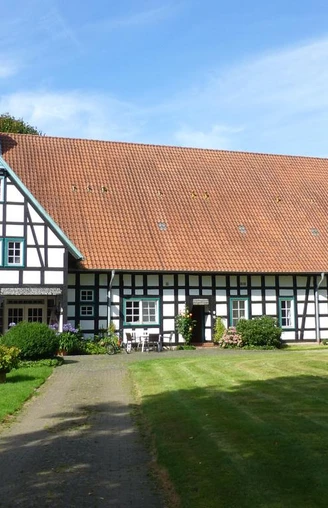 Fachwerkhaus auf gepflegtem Rasen, Hof Oberwahrenbrock, mit großen Dach und weiß-schwarzen Strukturen.