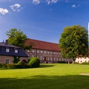 Historische Gebäude mit roten Ziegeldächern und grüne Wiese, blauer Himmel, Friedenspfahl.