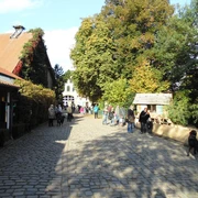 Tierpark Olderdissen, Bielefeld Ein sonniger Herbsttag auf einem Kopfsteinpflasterplatz, umgeben von alten Gebäuden und Bäumen, viele Besucher.
