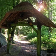 Waldlehrpfad Vosspäddken in der Erlebnisregion Artland Holztor im Wald mit Strohdach unter Bäumen, Sonnenlicht fällt durch das Blätterdach.