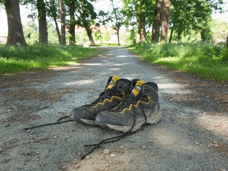 Durch die Allee aufs Kloster Clarholz zu: schön! Ein Paar abgenutzte Wanderstiefel liegt auf einem Schotterweg, umgeben von hohen, grünen Bäumen.