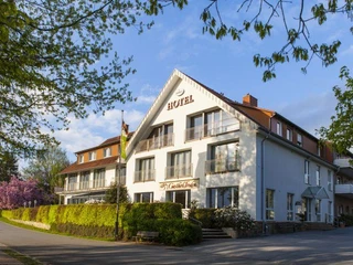 Landidyll Hotel Gasthof zum Freden Hotel in einem großen, weißen Gebäude mit Schrägdach, umgeben von Bäumen und blühenden Sträuchern.