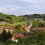 Borgholzhausen Ein idyllisches Dorf mit Kirchturm, umgeben von grünen Feldern und bewaldeten Hügeln im Hintergrund.