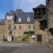 Mittelalterliche Burg mit Zinnen und Türmen, Steinwände, Statue im Innenhof, blauer Himmel.