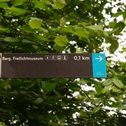 Wegweiser am Panoramasteig <p>Wegweiser zeigt Richtung Berg. Freilichtmuseum, Entfernung 0,1 km, umgeben von grünem Laub.</p>