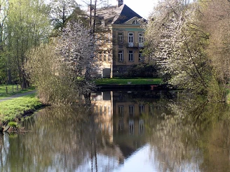 Schloss Hagenburg Schloss Hagenburg spiegelt sich im ruhigen Wasser, umgeben von blühenden Bäumen und üppigem Grün.