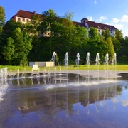 Kneipp-Erlebnispark in Bad Iburg: die Lehre von Sebastian Kneipp neu interpretiert.  Springbrunnen vor einem weitläufigen, historischen Gebäude mit rotem Dach und grüner Umgebung.