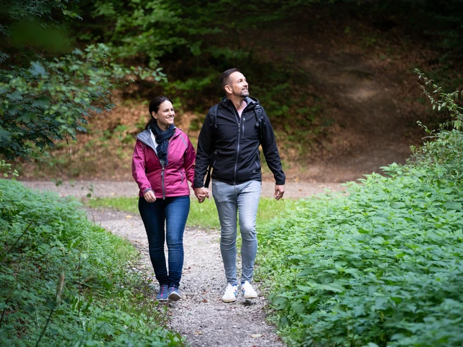 Ein paar genießt einen Spaziergang auf einem Waldweg, umgeben von üppigem Grün.