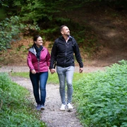 Wandern im Teutoburger Wald  Ein paar genießt einen Spaziergang auf einem Waldweg, umgeben von üppigem Grün.