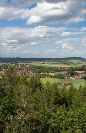 Weitblicke Landschaft von Wäldern und Feldern in sanften Hügeln unter blauem Himmel mit weißen Wolken.