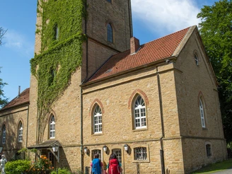 Diedrichsburg Zwei Personen spazieren zu einem historischen Gebäudeturm, überwuchert mit grünem Efeu.