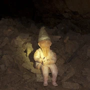 Ein Hüggelzwerg Ein Zwerg mit Spitzhut sitzt auf Steinbrocken in einer dunklen Höhle.