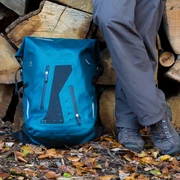 Wanderrast Ein blauer Wanderrucksack und Beine einer Person stehen auf buntem Herbstlaub vor Holzstapeln.