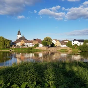 Blick auf das malerische Lüchtringen mit Kirche, Fachwerkhäusern und der Weser im Vordergrund.