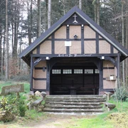 Waldbrauereiunterstand aus Holz und Ziegeln, umgeben von hohen Bäumen, mit hölzernem Zugang.
