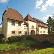 Klosterpforte Bersenbrück Historisches Gebäude mit Fachwerk, umgeben von gepflegtem Garten und einem kleinen Wasserlauf.