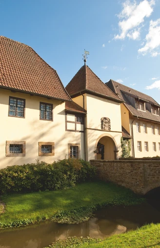 Klosterpforte Bersenbrück Historisches Gebäude mit Fachwerk, umgeben von gepflegtem Garten und einem kleinen Wasserlauf.