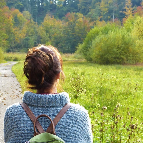 Wandern in Ankum Person mit Rucksack blickt auf herbstlichen Waldweg und grüne, bewaldete Landschaft.