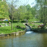 Grünes Stadtareal mit Bachlauf, Wiesen und Spaziergängern im westlichen Paderquellgebiet.