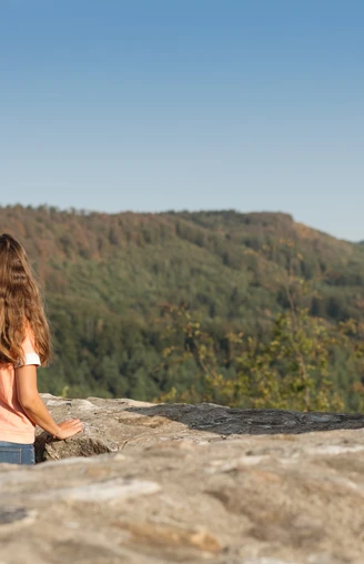 detmold-ruine-falkenburg-teutoburger-wald-tourismus-m-schoberer-4 Zwei Menschen genießen von einer Mauer am Berg aus den Blick auf die bewaldete Landschaft.