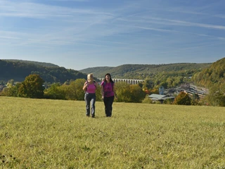 Altenbeken Zwei Frauen wandern über eine Wiese, im Hintergrund das Altenbeker Viadukt und bewaldete Hügel.