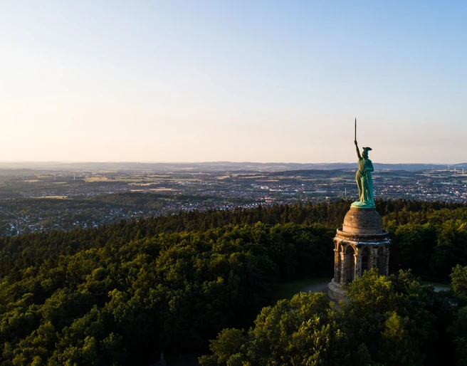 Hermannsdenkmal Hermannsdenkmal in einem bewaldeten Hügelplateau mit Blick auf die weitläufige Landschaft im Hintergrund.