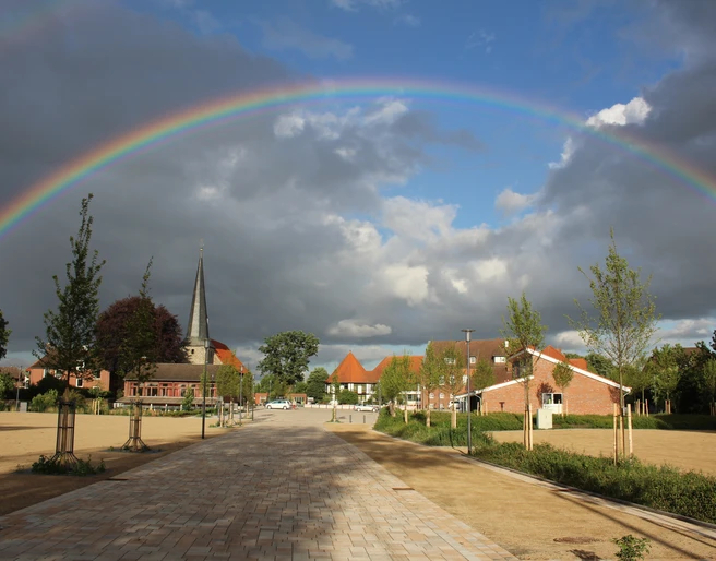 Stadtplatz Rehburg Ein weitläufiger Stadtplatz in Rehburg unter einem eindrucksvollen Regenbogen, mit Kirche und Häusern.